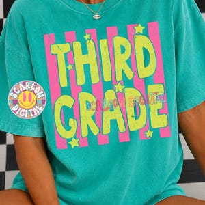 May include: A teal short-sleeve t-shirt featuring a graphic print with vertical hot pink stripes and the text THIRD GRADE in distressed lime green letters. The design includes small lime green star accents scattered across the front.
