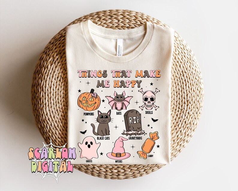 Puede incluir: Una camiseta blanca con un dise&ntilde;o gr&aacute;fico de tem&aacute;tica de Halloween. El texto "Things that make me happy" est&aacute; en la parte superior del dise&ntilde;o. El gr&aacute;fico incluye calabazas, murci&eacute;lagos, calaveras, un cementerio, gatos negros, fantasmas, brujas y caramelos.