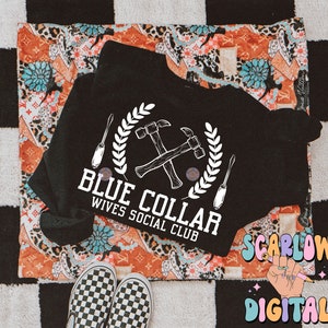 May include: Black t-shirt with a white graphic of crossed hammers and screwdrivers with a wreath around them. The text "Blue Collar Wives Social Club" is below the graphic.