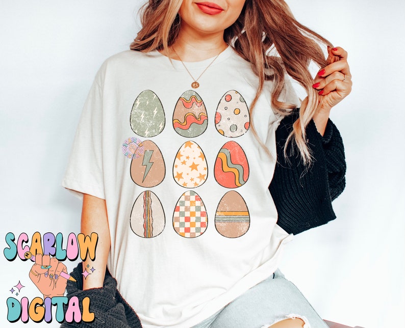 May include: A white t-shirt with a graphic of nine colorful Easter eggs with different patterns. The eggs are arranged in a 3x3 grid.