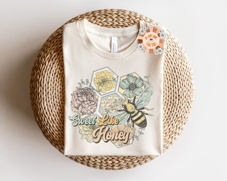 May include: A beige t-shirt with a graphic of a bee and flowers in a honeycomb pattern. The text "Sweet Like Honey" is printed in a retro font.