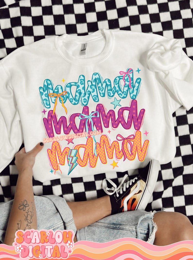 May include: White sweatshirt with the text "Mama Mama Mama" in colorful, stylized lettering. The text is decorated with stars, lightning bolts, and bows.