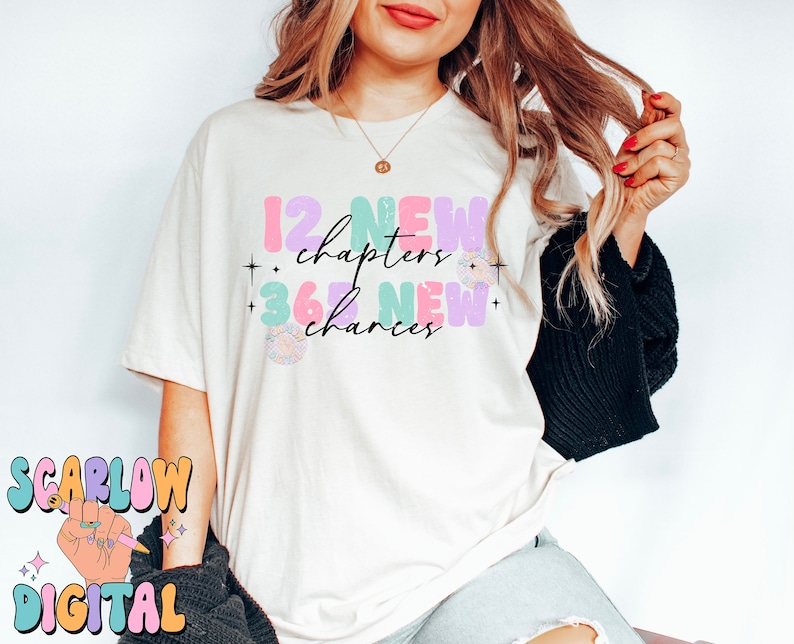 May include: A white t-shirt with the text "12 new chapters + 365 new chances" in colorful, bubbly letters. The text is decorated with stars and a small floral design.