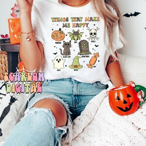 May include: White t-shirt with the text "Things that make me happy" and a graphic of Halloween icons including pumpkins, bats, black cats, ghosts, witches, candy, skulls, and graveyards.