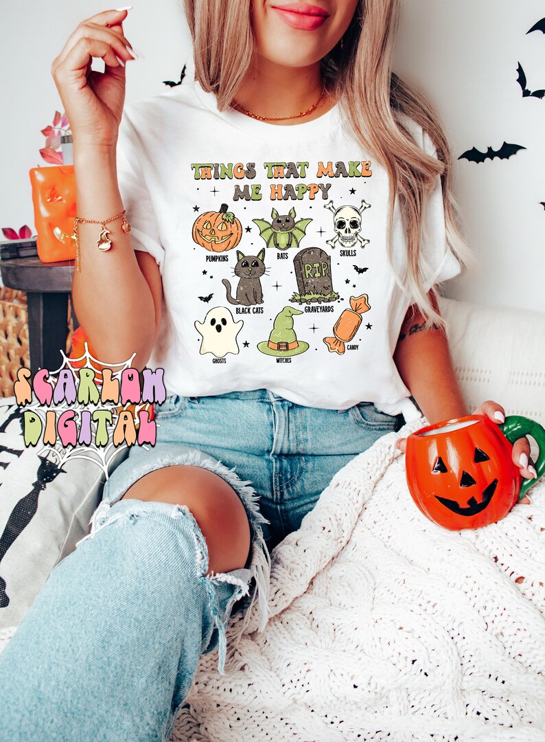 May include: White t-shirt with the text "Things that make me happy" and a graphic of Halloween icons including pumpkins, bats, black cats, ghosts, witches, candy, skulls, and graveyards.