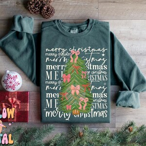 May include: A green sweatshirt with a Christmas tree design and the text "merry christmas" repeated multiple times in different variations.