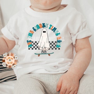 May include: White baby t-shirt with a graphic of a ghost skateboarding with the text "Let the spooky times roll" in a rainbow arch.