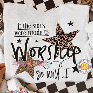 Pode incluir: Um moletom cinza claro com o texto "if the stars were made to Worship so will I." O design inclui estrelas pretas e duas formas de estrela, uma com estampa de leopardo e outra com glitter.