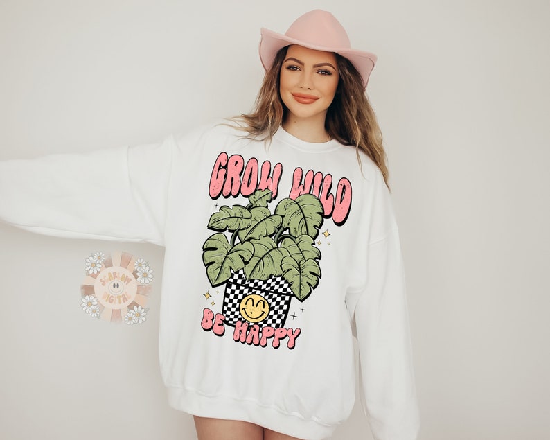 May include: White sweatshirt with a pink and green graphic of a plant in a pot with a smiley face and the text "Grow Wild Be Happy".