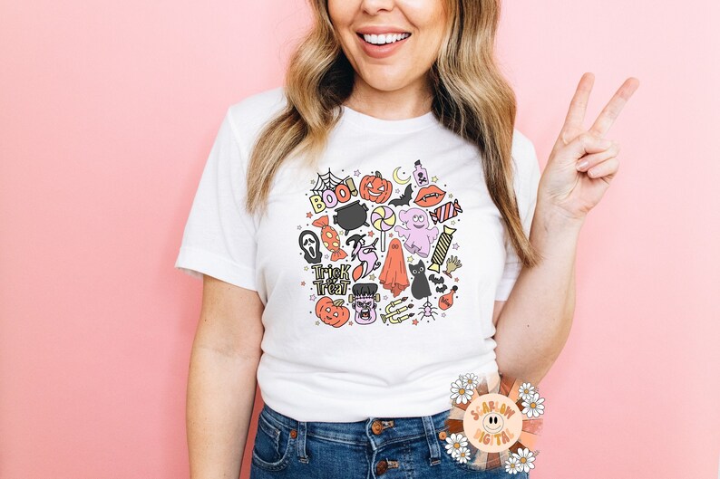 Peut inclure: Un t-shirt blanc avec un motif color&eacute; sur le th&egrave;me d'Halloween repr&eacute;sentant des fant&ocirc;mes, des citrouilles, des chauves-souris, des bonbons et le texte "Boo!" et "Trick or Treat".