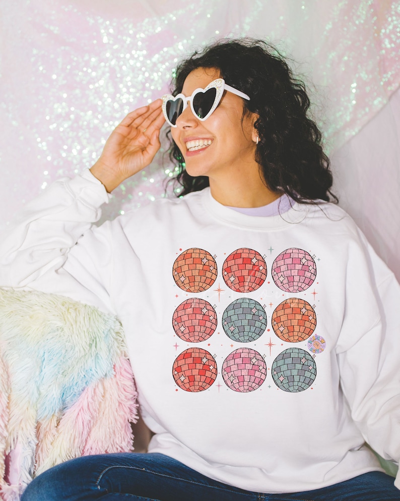 May include: White sweatshirt with a colorful design of nine disco balls. The disco balls are arranged in a 3x3 grid pattern. The sweatshirt has a crew neck and long sleeves.