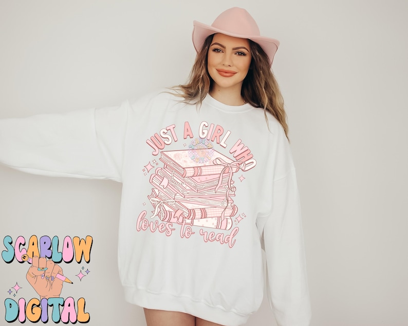 Puede incluir: Sudadera blanca con el texto "Just a girl who loves to read" y una pila de libros rosas con un dise&ntilde;o floral.