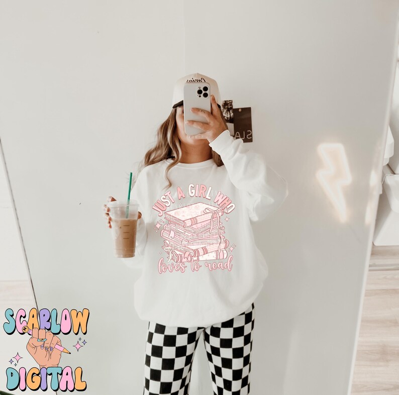 Puede incluir: Sudadera blanca con un gr&aacute;fico rosa de libros apilados y el texto "Just a girl who loves to read".