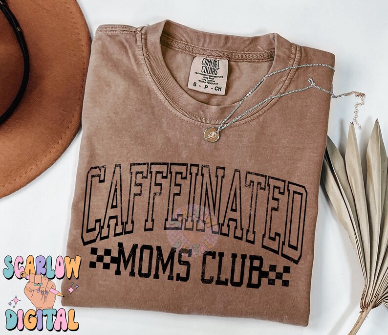 K&ouml;nnte beinhalten: Ein braunes T-Shirt mit dem Text "CAFFEINATED MOMS CLUB" in schwarzen Buchstaben. Das Shirt hat einen Used-Look und ist aus einem weichen, bequemen Stoff.