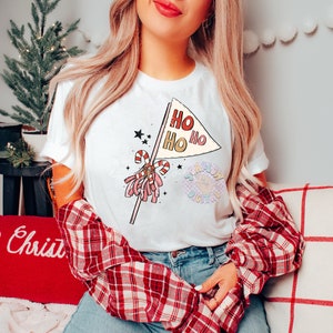 May include: A white t-shirt with a pink and red Christmas-themed graphic. The graphic features a candy cane and a flag with the text "Ho Ho Ho" on it.