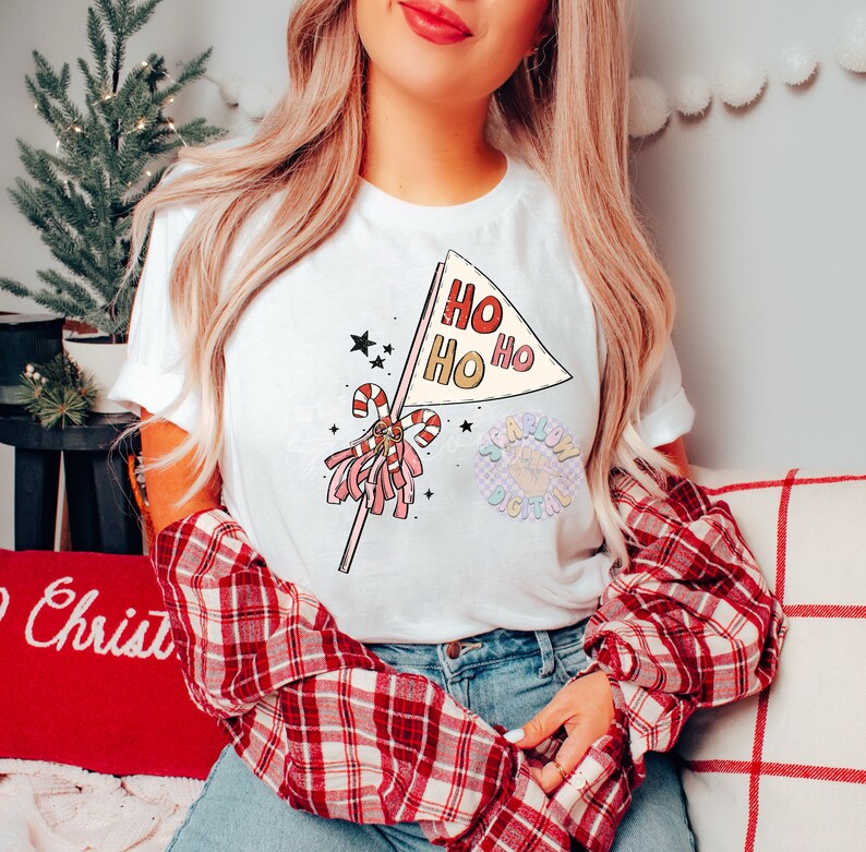 May include: A white t-shirt with a pink and red Christmas-themed graphic. The graphic features a candy cane and a flag with the text "Ho Ho Ho" on it.