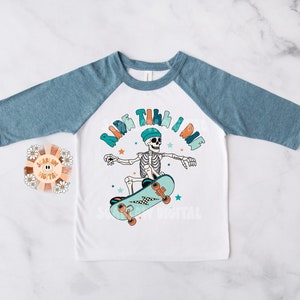 K&ouml;nnte beinhalten: Wei&szlig;es und blaues Baseball-T-Shirt mit einem Skelett, das Skateboard f&auml;hrt, und dem Text "Ride Til I Die".