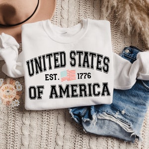 May include: White sweatshirt with a black graphic that says "UNITED STATES EST. 1776 OF AMERICA" with a small American flag graphic.