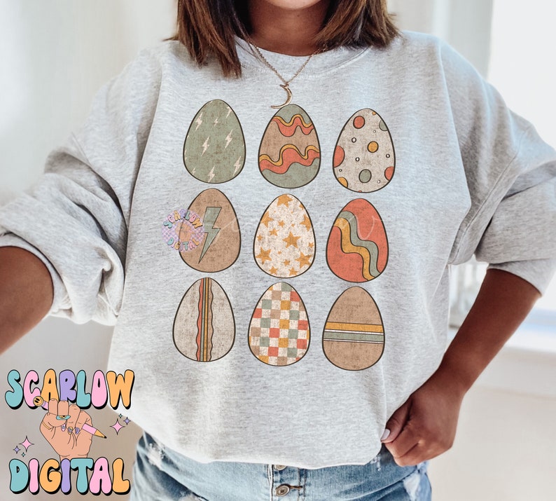 May include: A gray sweatshirt with a pattern of nine colorful Easter eggs. Each egg has a different design, including stripes, polka dots, stars, and lightning bolts.
