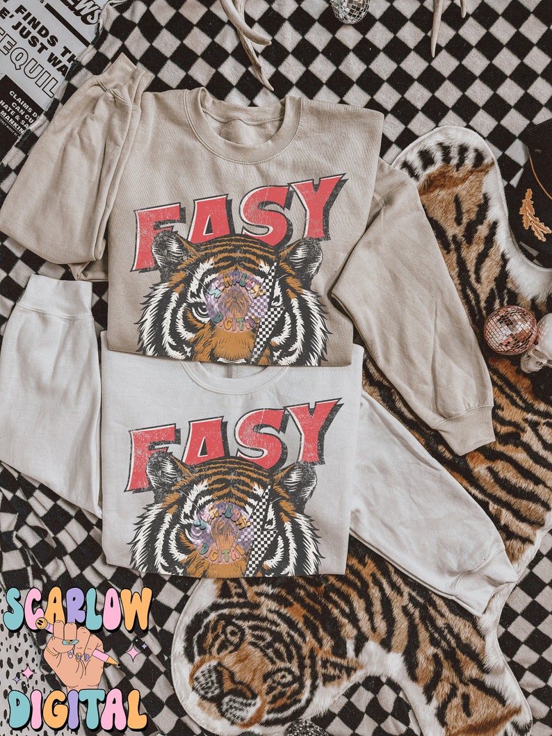 Puede incluir: Dos camisas beige de manga larga con un gr&aacute;fico de tigre y la palabra "EASY" en letras rojas. El tigre tiene un parche en el ojo a cuadros y detalles coloridos.