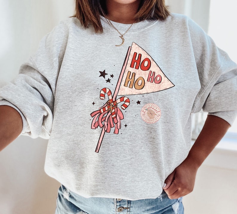 May include: A gray sweatshirt with a festive design featuring a pink and red pom-pom, candy canes, and a banner that reads "HO HO HO".
