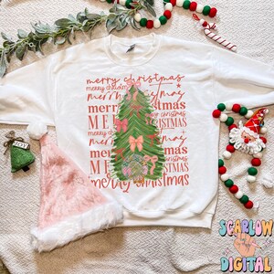 May include: A white sweatshirt with a pink and green Christmas tree design. The tree is surrounded by the words "merry christmas" repeated in different fonts and sizes.