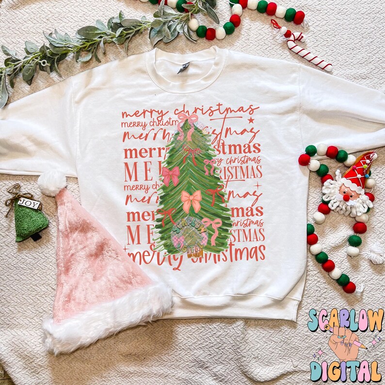 May include: A white sweatshirt with a pink and green Christmas tree design. The tree is surrounded by the words "merry christmas" repeated in different fonts and sizes.