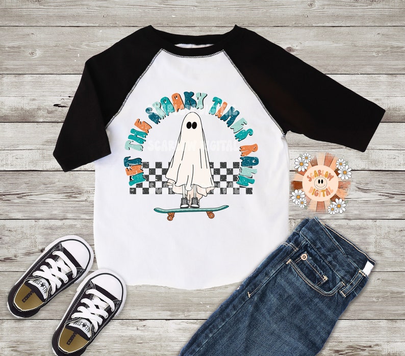 May include: A white baseball tee with black sleeves features a graphic of a ghost skateboarding with the text "Let the spooky times roll".