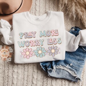 May include: White sweatshirt with the text "Pray More Worry Less" in pastel colors with a row of three pastel flowers below the text.