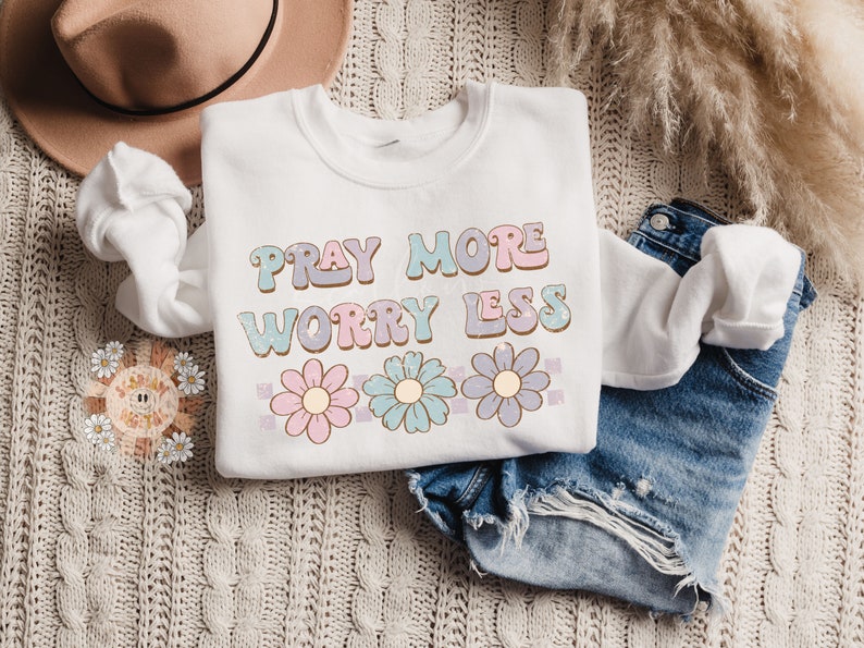 May include: White sweatshirt with the text "Pray More Worry Less" in pastel colors with a row of three pastel flowers below the text.