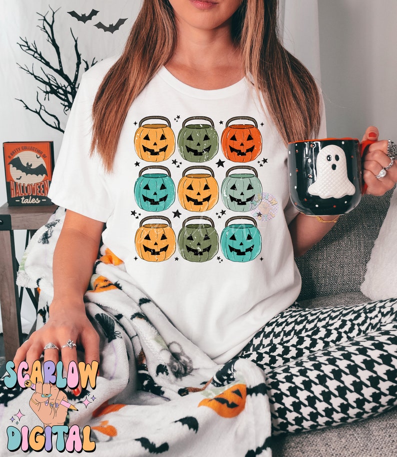 Puede incluir: Una camiseta blanca con un dise&ntilde;o de nueve cubos de calabaza de estilo vintage en varios tonos de naranja, verde y azul. Las calabazas tienen ojos, nariz y boca negros. El dise&ntilde;o est&aacute; centrado en la camiseta.