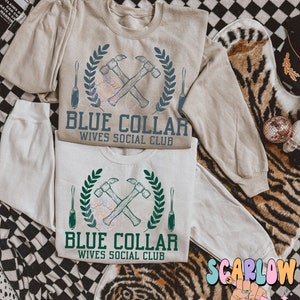 May include: A beige sweatshirt with a blue and green graphic design of crossed hammers and screwdrivers with a laurel wreath. The text "Blue Collar Wives Social Club" is printed below the graphic.