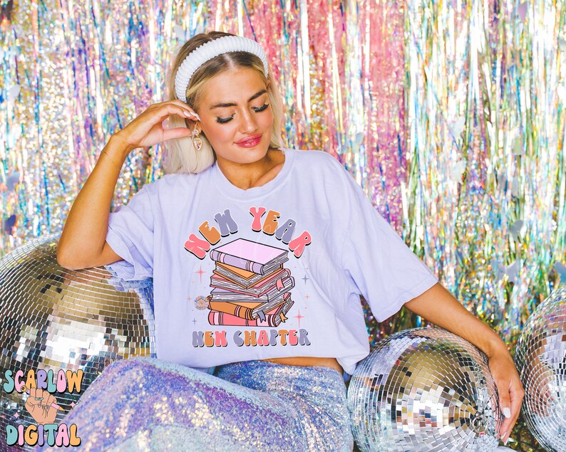 May include: A light purple t-shirt featuring a graphic of a stack of books and the text "New Year New Chapter".