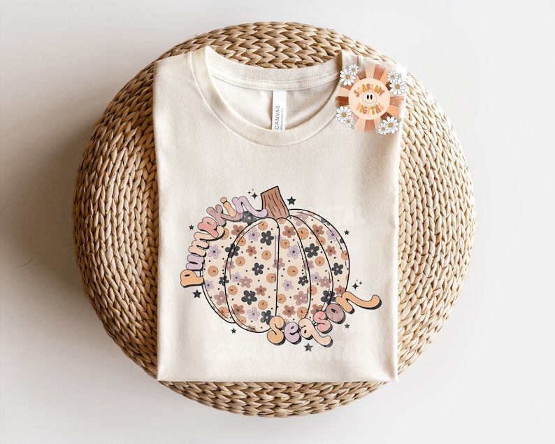 Pu&ograve; includere: Una maglietta beige con una grafica di una zucca con motivi floreali e il testo "pumpkin season" in un font retr&ograve;.