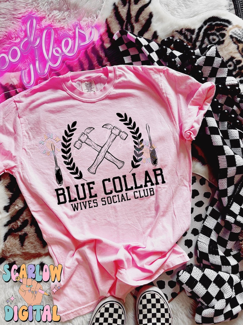 May include: Pink t-shirt with a black graphic of crossed hammers and a screwdriver with a wreath around them. The text "Blue Collar Wives Social Club" is below the graphic.