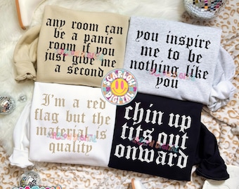May include: Four crewneck sweatshirts in beige, light grey, white, and black. The beige sweatshirt reads, any room can be a panic room if you just give me a second. The grey reads, you inspire me to be nothing like you. The white reads, I'm a red flag but the material is quality. The black reads, chin up tits out onward.