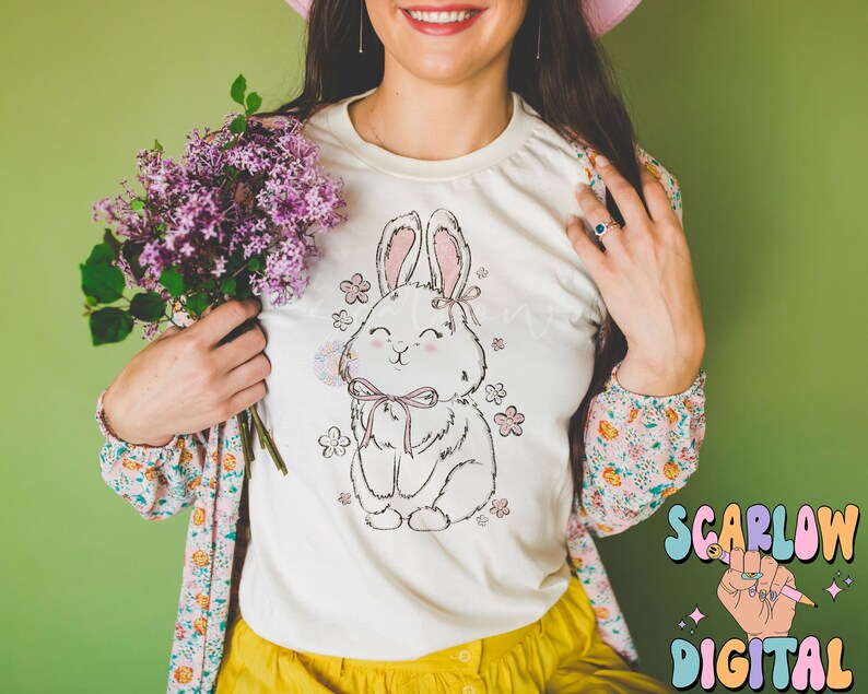 May include: White t-shirt with a pink and white bunny rabbit graphic with flowers and a pink bow. The bunny is holding a pink flower.