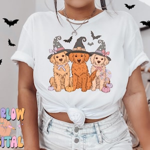 K&ouml;nnte beinhalten: Wei&szlig;es T-Shirt mit einem Motiv von drei Golden Retrievern, die Hexenh&uuml;te tragen und K&uuml;rbisse halten. Die Hunde tragen rosa und wei&szlig;e Schleifen.