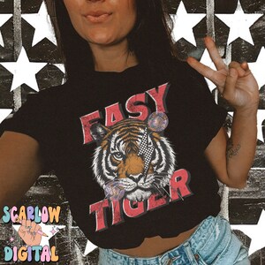 Puede incluir: Una camiseta negra con un gr&aacute;fico de un tigre con un rayo a trav&eacute;s de su ojo. El texto "EASY TIGER" est&aacute; impreso en rojo y blanco en la camiseta.