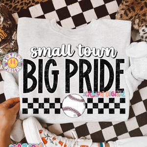 May include: A light gray sweatshirt with the text "small town BIG PRIDE" in black and white. A baseball graphic is centered below the text, with a black and white checkered pattern above and below the baseball.