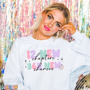 May include: White sweatshirt with a colorful graphic design that says "12 new chapters + 365 new chances".