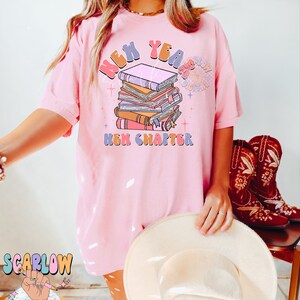 May include: Pink t-shirt featuring a graphic design of a stack of books with the text "New Year New Chapter".
