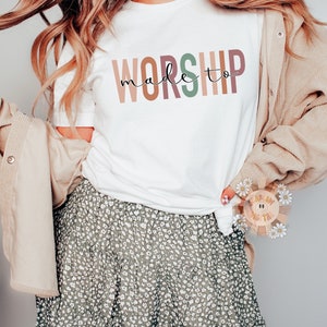 Op de afbeelding: Een wit T-shirt met de tekst "made to worship" in kleurrijke letters. De letters zijn in tinten roze, oranje, bruin, groen en geel.