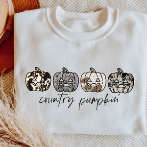 May include: White sweatshirt with a graphic of four cow print pumpkins with black outlines and the text "country pumpkin".