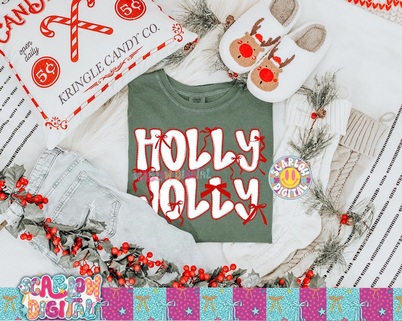 以下が含まれることがあります： お祝いのテーマのフラットレイ。白い文字と赤いリボンで「HOLLY JOLLY」と書かれた緑色のTシャツは、キャンディケインの枕、トナカイのスリッパ、赤いベリーで飾られたデニムジーンズに囲まれています。季節感のある居心地の良いシーンです。