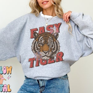 Puede incluir: Una sudadera gris con un gr&aacute;fico de la cara de un tigre y el texto "EASY TIGER" en letras rojas.