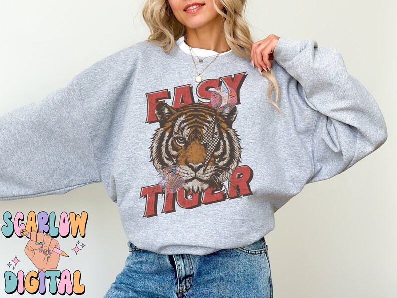 Puede incluir: Una sudadera gris con un gr&aacute;fico de la cara de un tigre y el texto "EASY TIGER" en letras rojas.