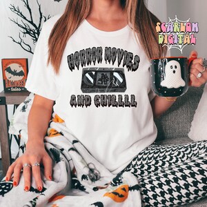 May include: A white t-shirt with the text "Horror Movies and Chilll" in black dripping letters. A vintage VHS cassette tape is depicted in the center of the text.
