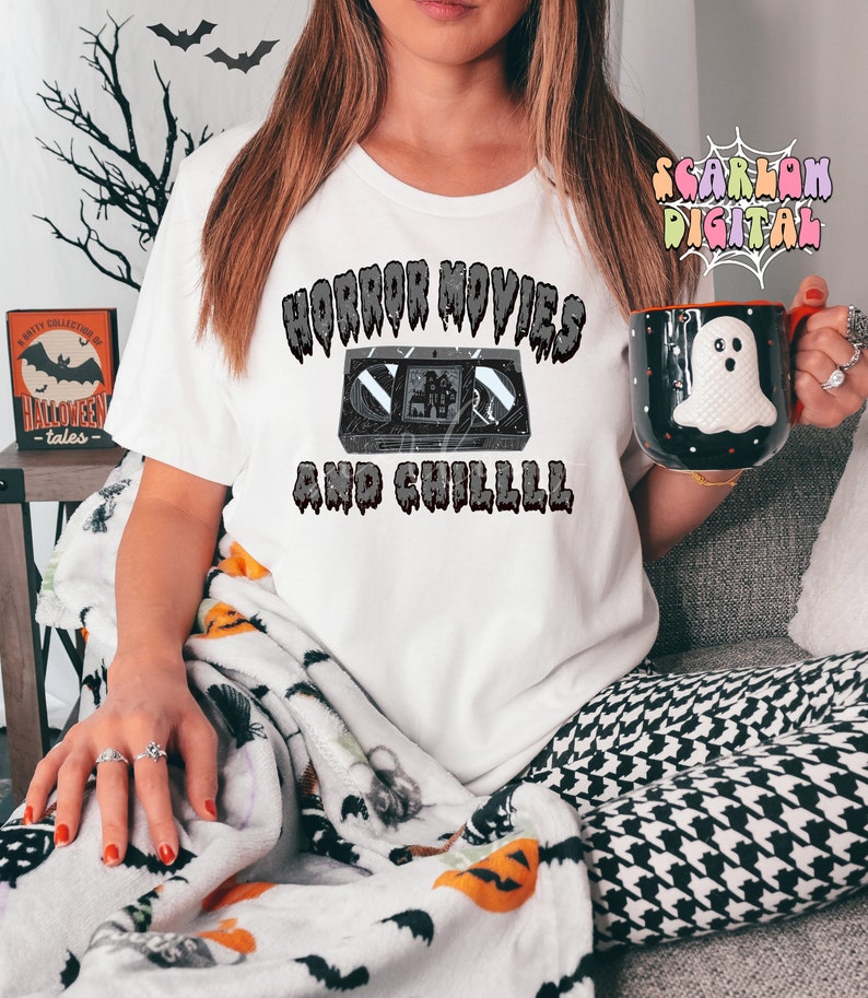 May include: A white t-shirt with the text "Horror Movies and Chilll" in black dripping letters. A vintage VHS cassette tape is depicted in the center of the text.