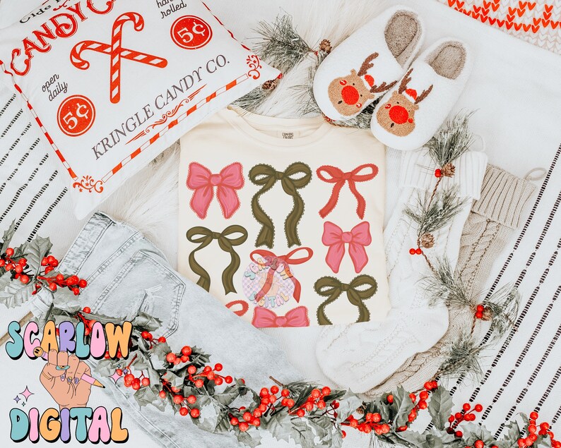 May include: A white t-shirt with a festive design of red and green bows. The shirt is surrounded by holly, a white knitted stocking, and a pillow with the text "Kringle Candy Co."